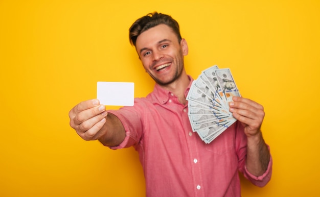 Un bell'uomo moderno di successo mostra la carta di credito e un sacco di soldi sulla fotocamera per lo shopping online