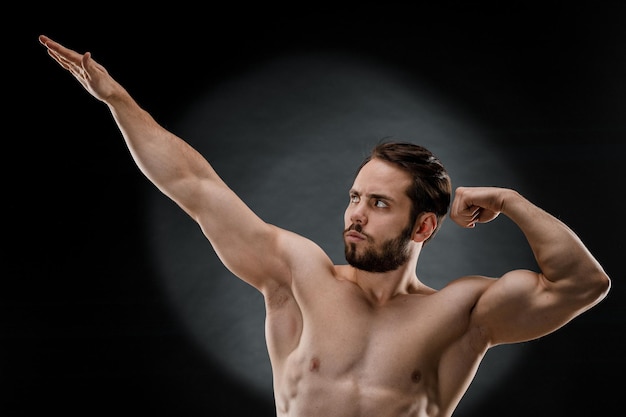 Un bell'uomo muscoloso senza maglietta posa per un fotografo in uno studio fotografico scuro Il concetto di sport