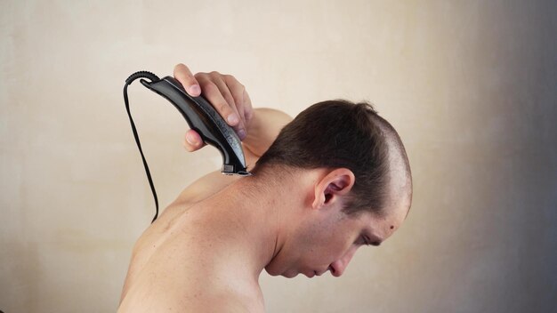 Un bell'uomo si taglia i capelli con un rifinitore una macchina a casa Selfservice durante l'isolamento della quarantena Rimani a casa parrucchiere