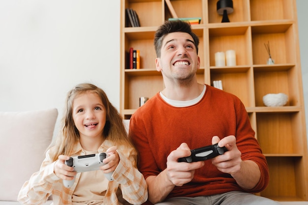 Un bell'uomo sorridente e sua figlia giocano a videogiochi con un joystick seduti a casa