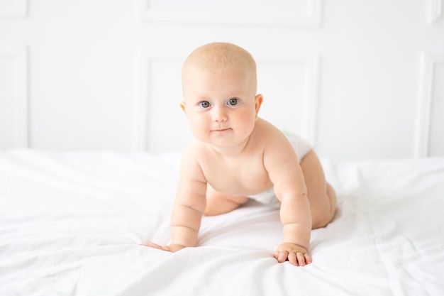 Un bellissimo bambino sano e allegro in un pannolino è seduto su un letto con biancheria da letto bianca il bambino sta guardando la telecamera