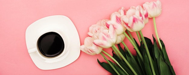 Un bellissimo bouquet di delicati tulipani rosa accanto a una tazza di caffè su uno sfondo rosa Potrebbe esserci il tuo testo Spazio orizzontale per la copertina del sottotitolo della foto