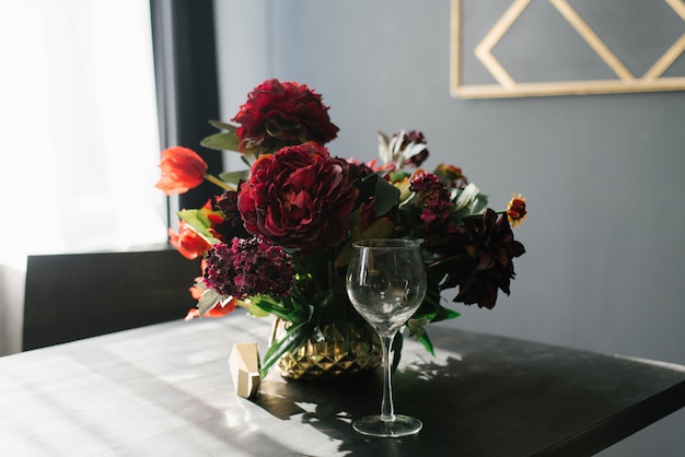 Un bellissimo bouquet di peonie bordeaux in un vaso sul tavolo del soggiorno con pareti nere e un bicchiere sul tavolo