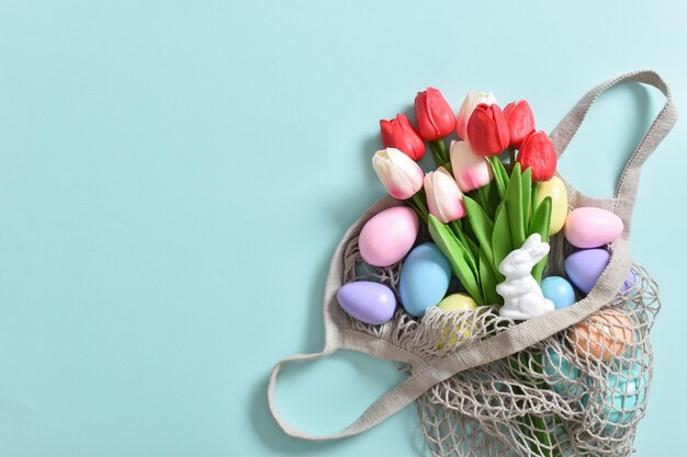 Un bellissimo bouquet di tulipani con un sacchetto di corda contenente uova dipinte Banner per le vacanze di Pasqua Felice Spazio di copia Vista dall'alto piatta