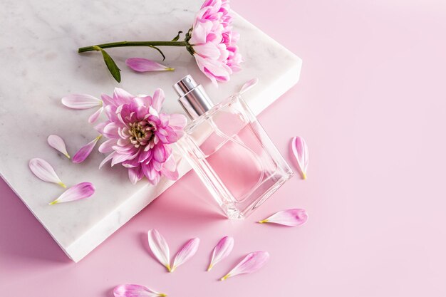 Un bellissimo flacone trasparente con un rimedio cosmetico naturale spray o profumo appoggiato su un podio di marmo bianco con petali e boccioli di fiori