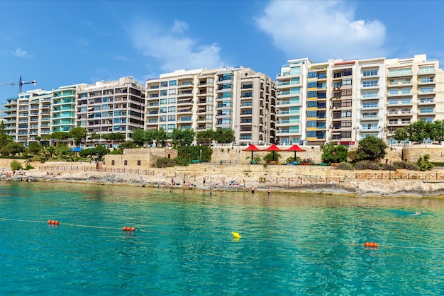 Un bellissimo paesaggio urbano con una spiaggia di sabbia e edifici residenziali sullo sfondo del cielo nuvoloso blu.