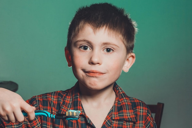 Un bellissimo ragazzino in pigiama sorride e tiene in mano uno spazzolino da denti su uno sfondo verde