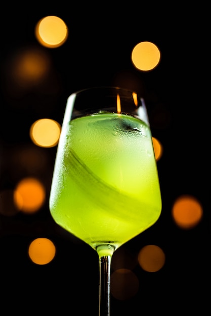 Un bello cocktail verde chiaro con sedano in un bicchiere di vino, luci del bokeh, fuoco selettivo