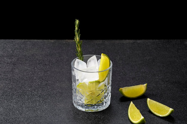 Un bicchiere con ingredienti ghiaccio e limone per la preparazione di cocktail e bevande, su sfondo nero