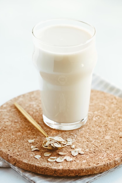 Un bicchiere con latte d'avena fatto in casa e cucchiaio con scaglie su un vassoio in cucina Il concetto di cibo vegetariano e sano
