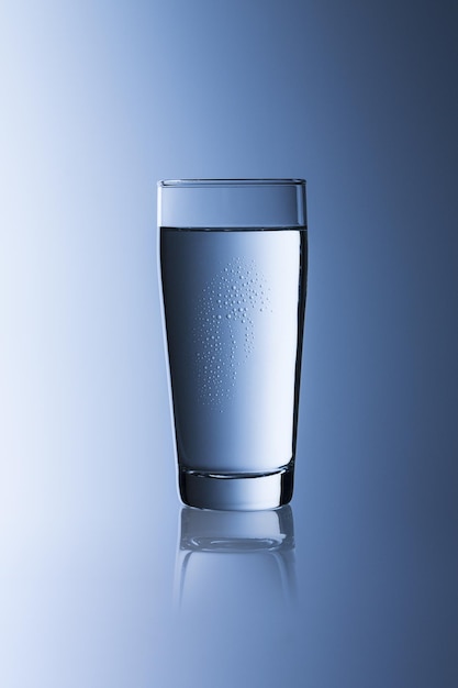Un bicchiere d'acqua con acqua potabile su sfondo blu sfumato Willi Cup con la riflessione