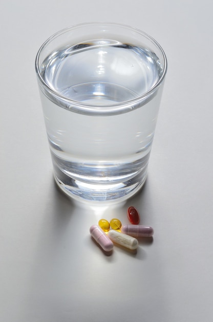 Un bicchiere d'acqua potabile e diverse capsule con vitamine. sfondo chiaro. avvicinamento.