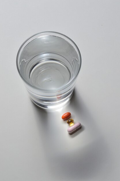 Un bicchiere d'acqua potabile e diverse capsule con vitamine. sfondo chiaro. avvicinamento.