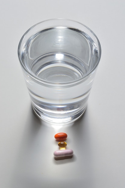 Un bicchiere d'acqua potabile e diverse capsule con vitamine. sfondo chiaro. avvicinamento.