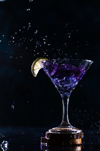 Un bicchiere da cocktail con un drink all'interno si trova su un supporto con una fetta di lime sul bordo della scia al neon dietro il bicchierino