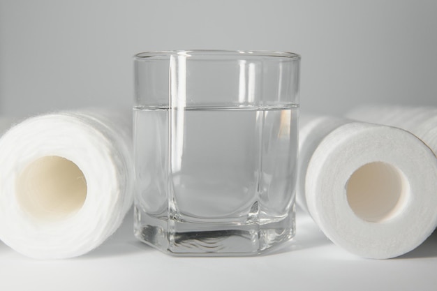 Un bicchiere di acqua potabile e cartucce filtranti su sfondo bianco