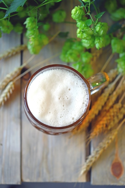 Un bicchiere di birra di frumento su una superficie di legno. Spighe di grano e luppolo.
