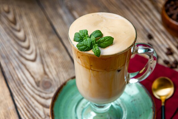 Un bicchiere di caffè con latte decorato con foglie di menta sul tavolo, caffè dalgona, da vicino.