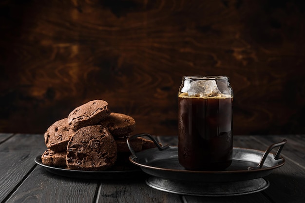 Un bicchiere di caffè ghiacciato nero e biscotti al cioccolato su un piatto.