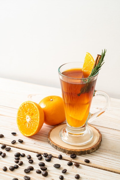 Un bicchiere di caffè nero americano ghiacciato e uno strato di succo d'arancia e limone decorato con rosmarino e cannella sul tavolo di legno