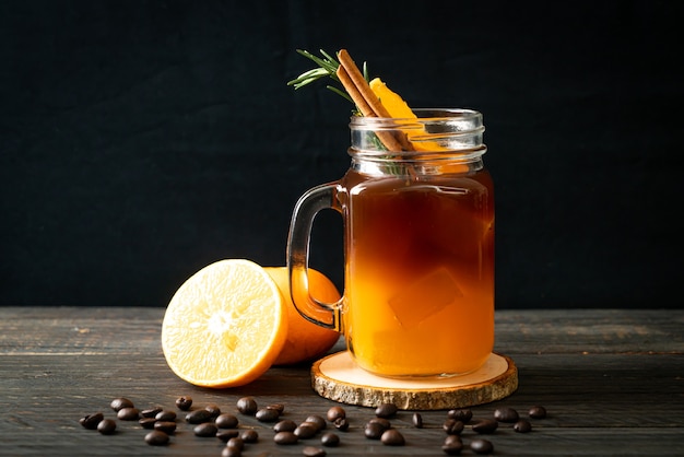 Un bicchiere di caffè nero americano ghiacciato e uno strato di succo d'arancia e limone decorato con rosmarino e cannella