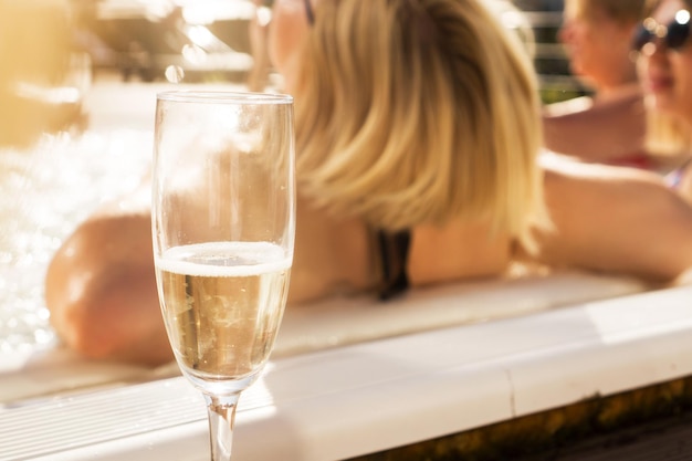 Un bicchiere di champagne a bordo piscina in una giornata di sole. Sfondo sfocato con donna indietro