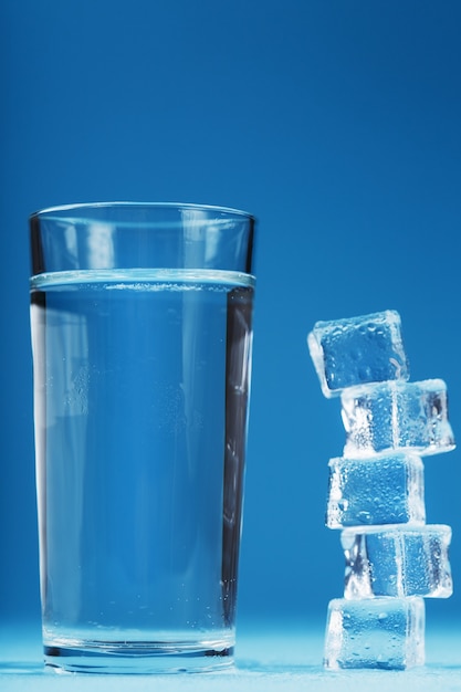 Un bicchiere di ghiaccio e acqua limpida, cubetti di ghiaccio su sfondo blu. Una bevanda rinfrescante nelle giornate calde. Spazio libero
