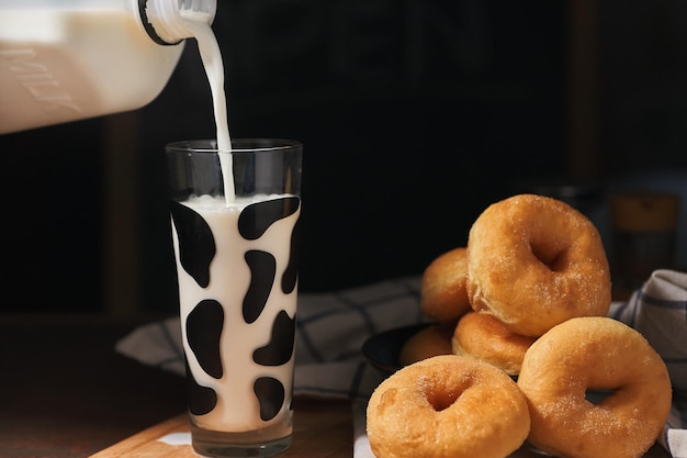 Un bicchiere di latte viene versato in un bicchiere con un mucchio di ciambelle sul tavolo.