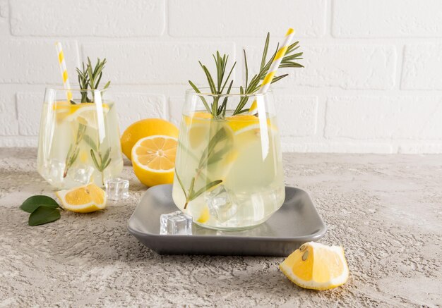 Un bicchiere di limonata fatta in casa con cubetti di ghiaccio su un piatto di ceramica e un tavolo grigio cemento deliziosa bevanda estiva senza conservanti e coloranti