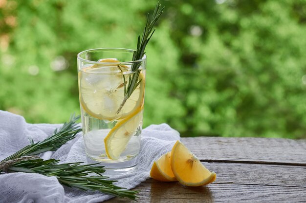 Un bicchiere di limonata fredda, spicchi di limone su uno sfondo di fogliame verde