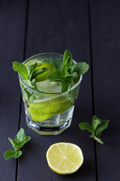 Un bicchiere di mojito freddo con lime, limone e menta su uno sfondo di legno nero Primo piano di un cocktail rinfrescante