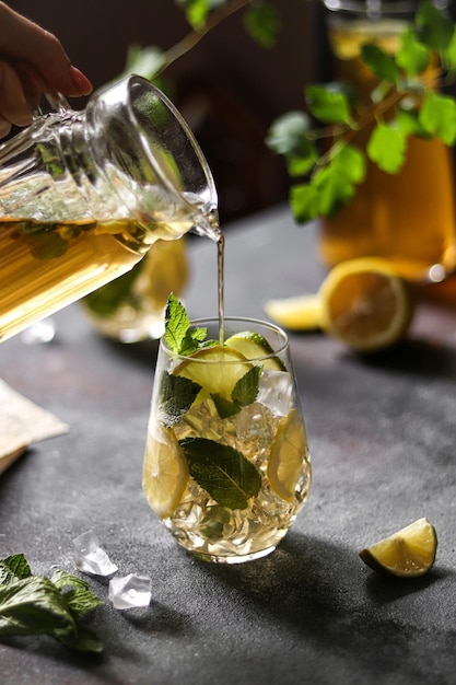 Un bicchiere di mojito viene versato in un bicchiere con fettine di limone e foglie di menta.