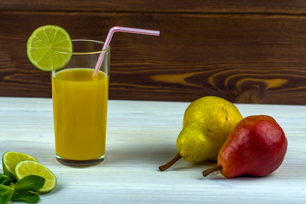 Un bicchiere di succo d&#39;arancia appena spremuto. Ramoscelli di menta e fettine di lime e due pere.