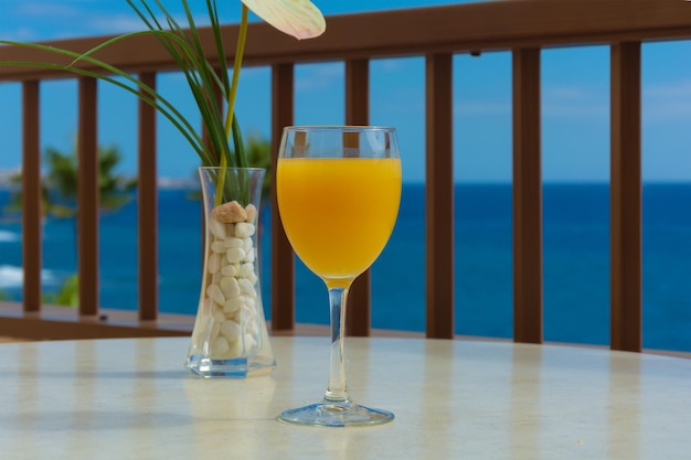 Un bicchiere di succo d'arancia e un vaso di erba verde stanno sul tavolo contro il mare blu