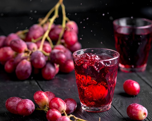 Un bicchiere di succo d'uva fresco, conserve di succo d'uva. Sfondo scuro, schizzi e gocce in un bicchiere.