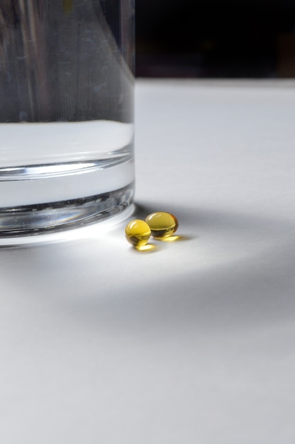 Un bicchiere di vetro e due compresse gialle con vitamine. avvicinamento.