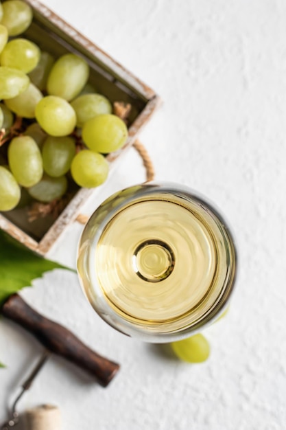 Un bicchiere di vino bianco su sfondo bianco testurizzato con cavatappi e uva Vista dall'alto Copia spazio