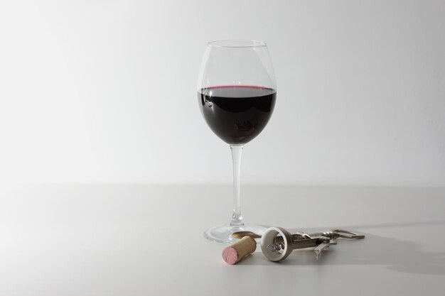un bicchiere di vino e alcuni strumenti per il vino su una superficie di legno bianco vino rosso