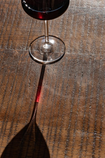 Un bicchiere di vino rosso su una superficie di legno bicchiere di vino con la sua ombra