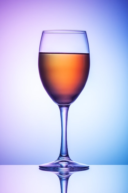 Un bicchiere di vino si trova su un tavolo su uno sfondo blu-viola.