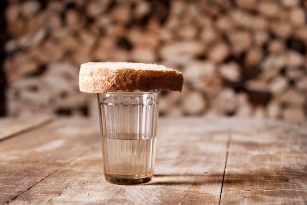 Un bicchiere di vodka e un pezzo di pane su un tavolo di legno e legna da ardere dietro