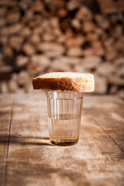 Un bicchiere di vodka e un pezzo di pane su un tavolo di legno e legna da ardere dietro
