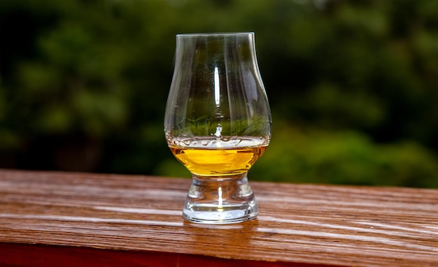 Un bicchiere di whisky si trova su un tavolo di legno con uno sfondo verde.