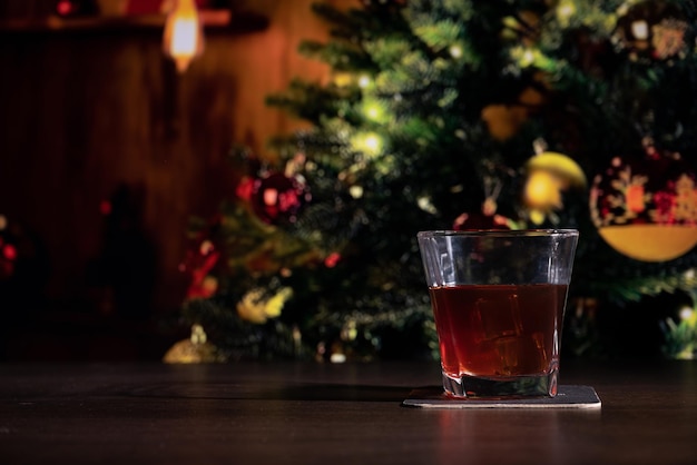 Un bicchiere di whisky sul bar di fronte all'immagine sfocata camera di casa di Natale con albero e illuminazione bokeh festiva sfocata sullo sfondo delle vacanze