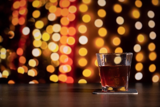 Un bicchiere di whisky sul bar di fronte all'immagine sfocata camera di casa di Natale con albero e illuminazione bokeh festiva sfocata sullo sfondo delle vacanze