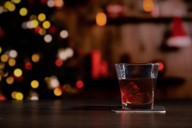 Un bicchiere di whisky sul bar di fronte all'immagine sfocata camera di casa di Natale con albero e illuminazione bokeh festiva sfocata sullo sfondo delle vacanze