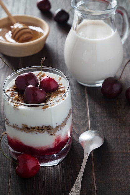 Un bicchiere di yogurt alla ciliegia con muesli, miele e un barattolo di latte