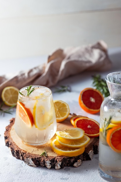 Un bicchiere e una caraffa di limonata Fette di limone e pompelmo con foglie di rosmarino in una bevanda