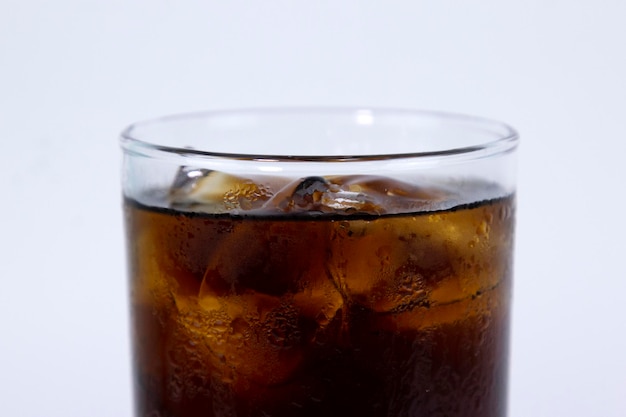 Un bicchiere isolato di cola nera con ghiaccio viene riempito su sfondo bianco
