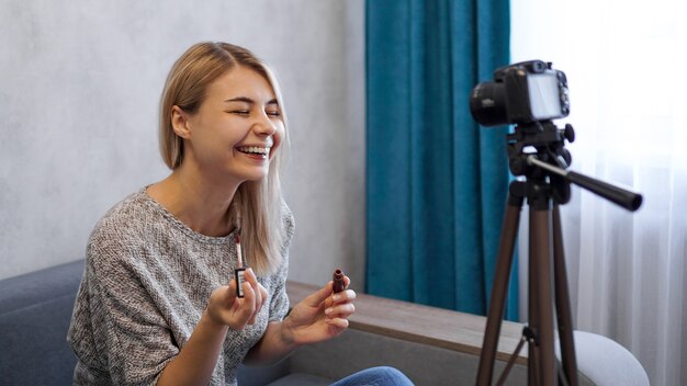 Un blogger di bellezza o un video blogger racconta e mostra agli abbonati come truccarsi. La giovane donna dipinge le labbra e ride a uno scherzo